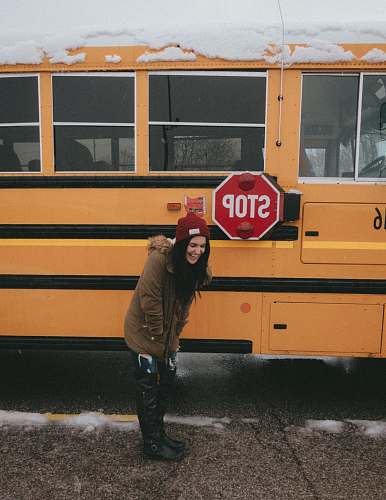 human woman in brown parka coat standing in front of yellow bus people