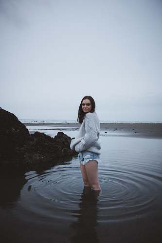 human woman in gray sweater standing on shallow sea water under gray sky people