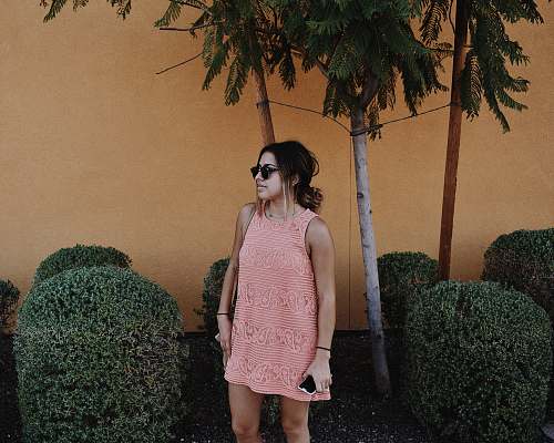 people woman in pink sleeveless shift mini dress standing near bushes at daytime human