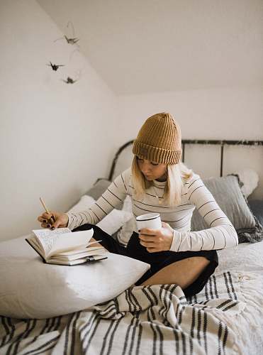 people woman in striped shirt sitting on bed while writing human
