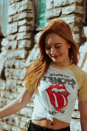 female woman in white and brown crew-neck T-shirt standing beside wall woman