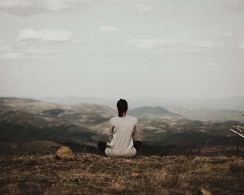 people woman sitting on cliff overlooking mountains during daytime human