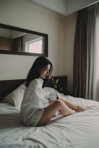 people woman sitting on white bed holding flower human