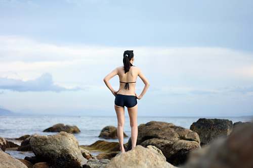 swimwear woman standing on stones near body of water bikini