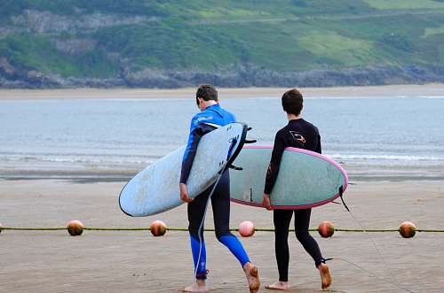 water two men walking on the seashore carrying surfboards ocean