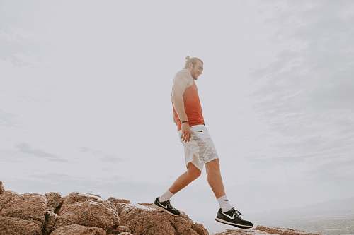 clothing man wearing orange tank top standing on brown rocks shorts