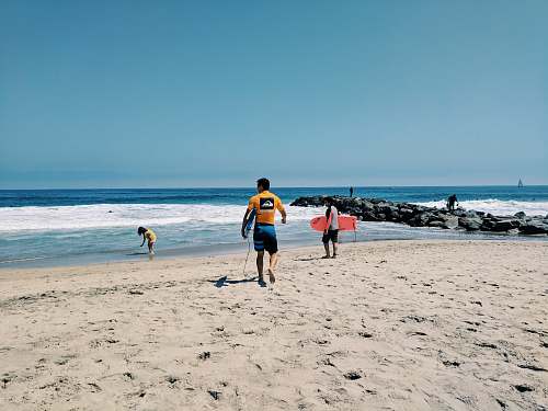 clothing two person walking on beach shore holding bodyboards shorts