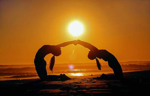 morocco silhouette of two woman bending while holding hands during sunset yoga