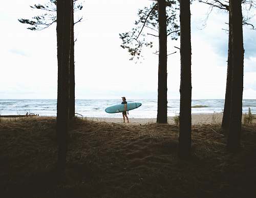 ocean person standing while carrying blue surfboard near sea during daytime coast