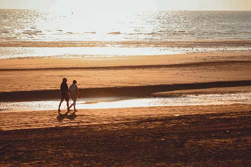 coast two person walking beside beach ocean