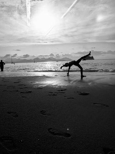 nature grayscale photography of person bending on shore during daytime ocean