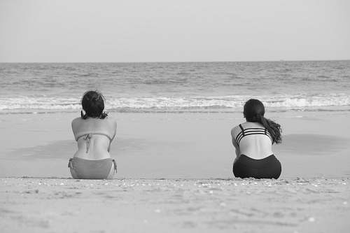 sea two women sitting on shore front of calm sea water