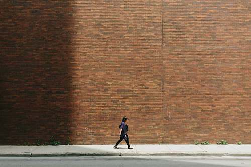 wall woman in black shirt walking on sidewalk near brown concrete wall partition brick