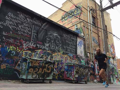 street man in black shirt running near wall with graffiti wall