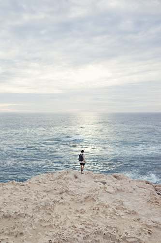 ocean person standing on the edge of the cliff near ocean sea
