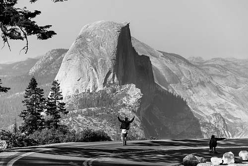 black-and-white grayscale photo of man standing on asphalt road fornt of mountain grey