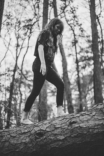 person grayscale photo of woman walking on log black-and-white