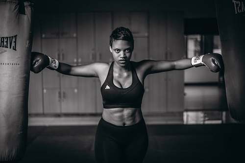 person grayscale photo of woman with gloves touching heavy bags fitness