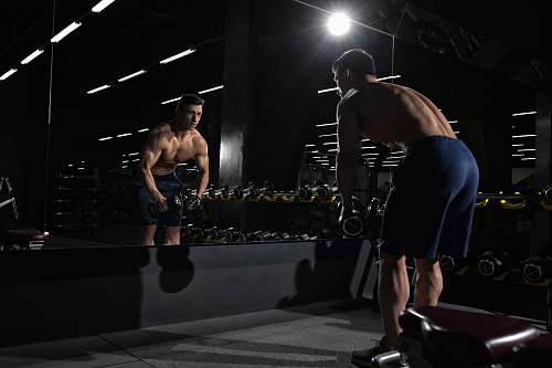 person man carrying dumbbell standing in front of mirror sport
