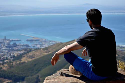 person man in black shirt and blue bottom sitting on rock outdoors