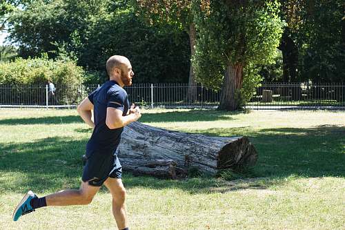 person man in blue t-shirt and blue shorts running near log shorts