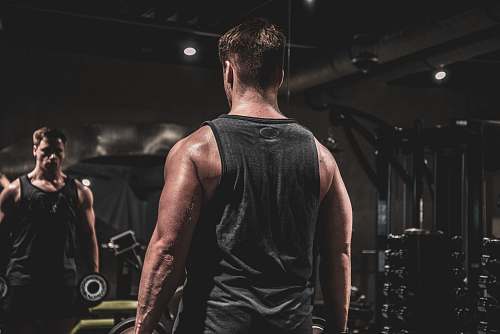 person man in gray tank top doing exercise holding weight inside gym exercise