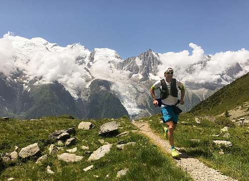 people man in white shirt and blue shorts running on brown ground between green grass during daytime mountain