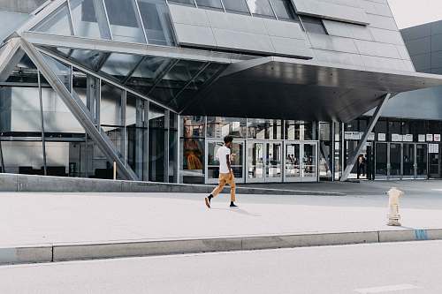 person man in white t-shirt walking beside building during daytime architecture