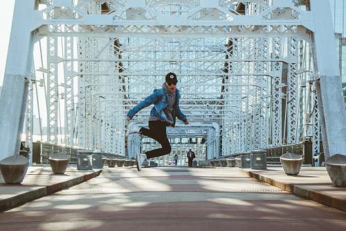 person man jumping on grey and white bridge during daytime people
