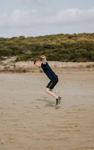 person man jumping on sand at daytime people