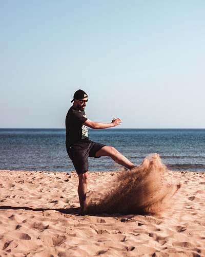 person man kicking a sand beside seashore during daytime nature