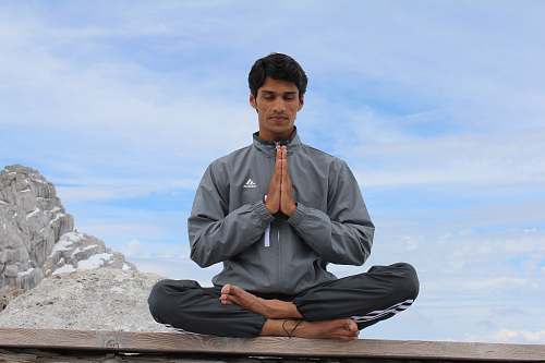 person man meditating on brown wooden platform during daytime exercise