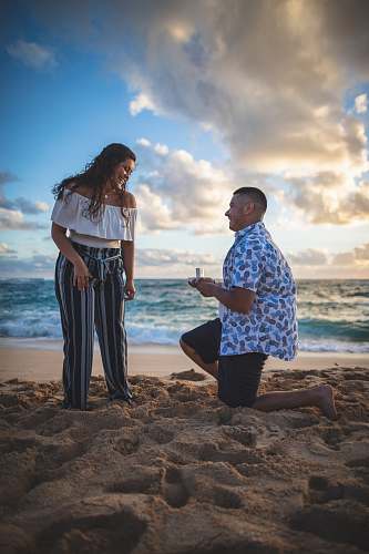 person man proposing on woman on beach apparel