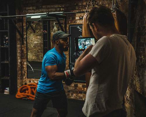 person man punching heavy bag near standing man sports