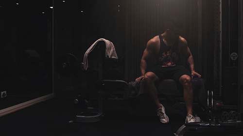 person man wearing black tank top sitting on the weight bench footwear