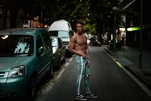 person man wearing blue Amiri denim track pants standing beside green car car