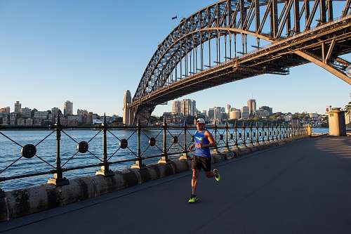 person man wearing blue tank top running under bridge building