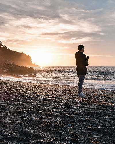 people man wearing jacket standing on beach during golden hour person