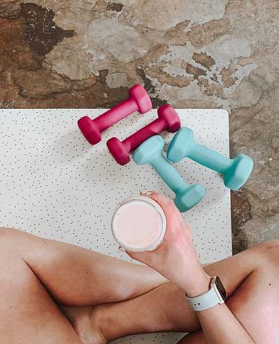 person person holding white liquid filled cup above two pairs of dumbbells fitness
