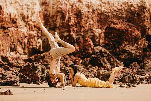 person photography of woman lying on sand in front of man during daytime stretch