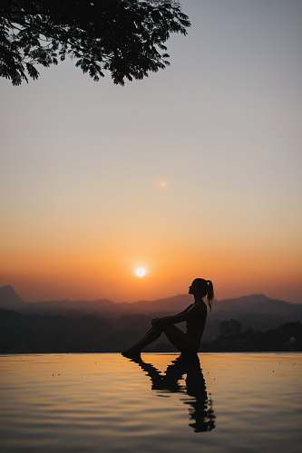 person silhouette of woman sitting on edge of eternity pool during golden hour outdoors