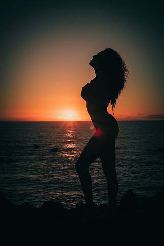 person silhouette of woman standing beside sea during golden hour nature