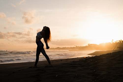 people silhouette of woman stretching her arms on seashore during sunrise person