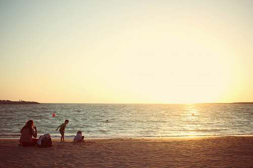 person three people sitting near seashore during daytime nature