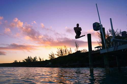 person topless man jumping on lake under orange and blue skies exuma