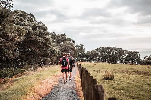 person two men walking on dirt trail beside brown fence sport