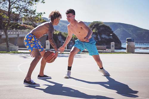 person two topless men playing basketball during daytime people