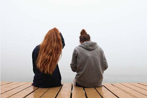 person two women sitting on wooden dock over body of water people