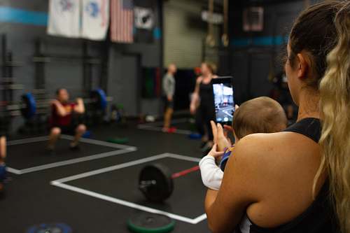 person woman carrying baby while using smartphone inside gym gym