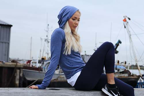 person woman in blue hoodie and black leggings lounging at gray concrete surface working out